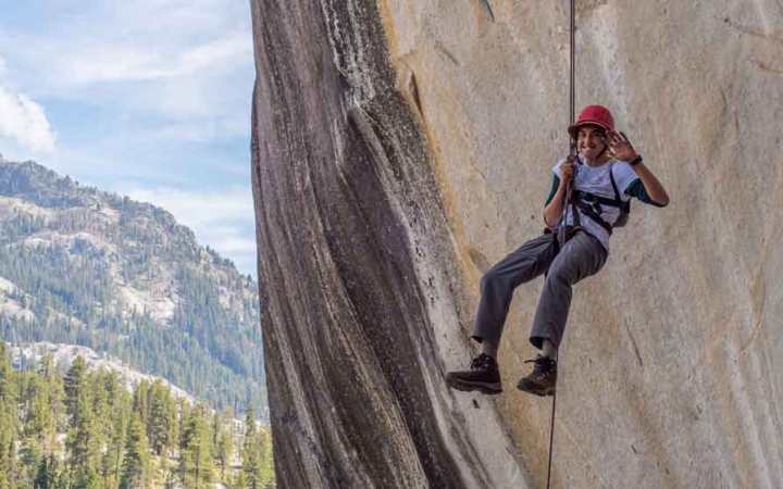 A student pauses to smile at the camera while rappelling down a rock wall 